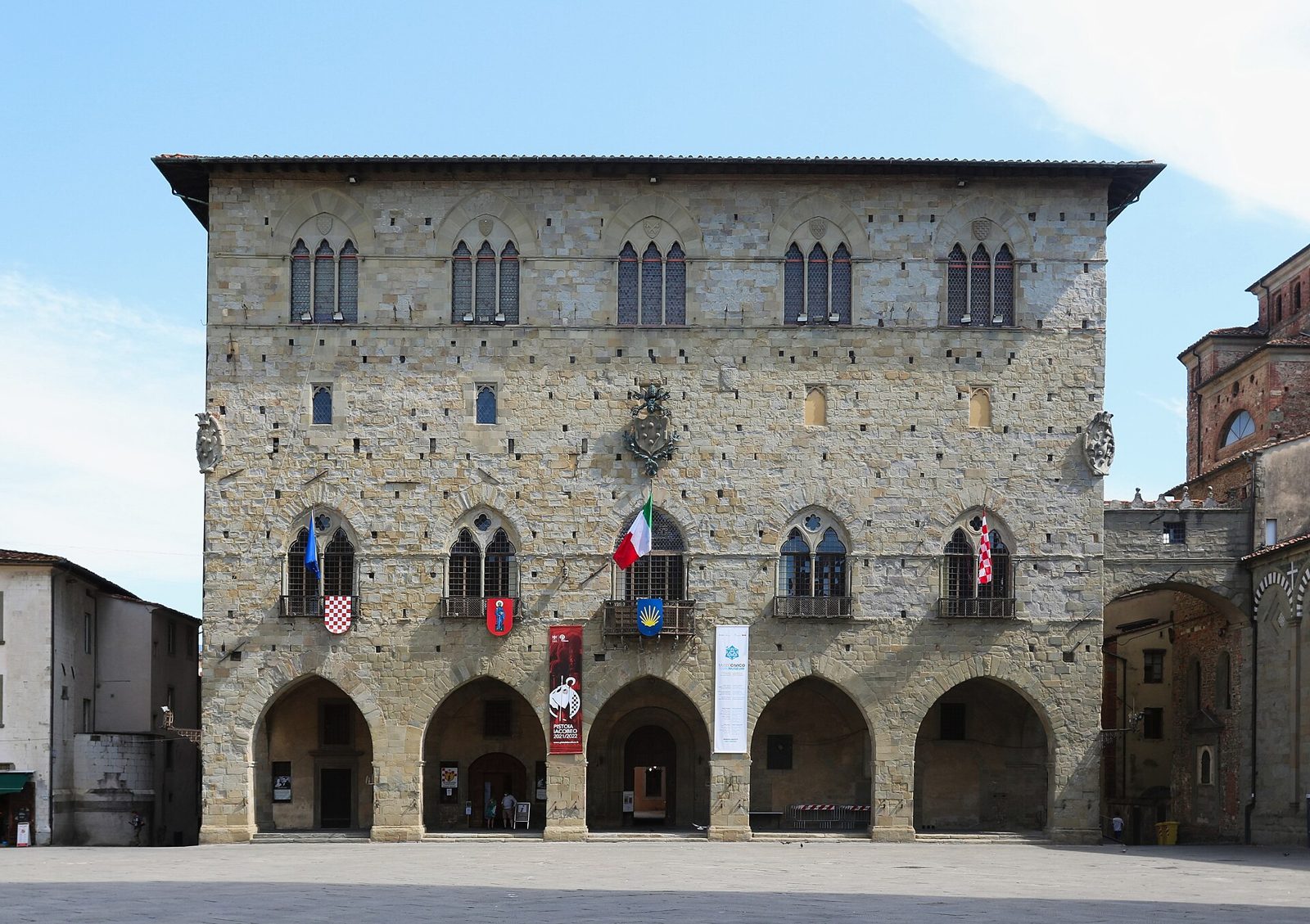 La facciata in pietra del Palazzo Comunale di Pistoia con il porticato e le bandiere, in Piazza del Duomo