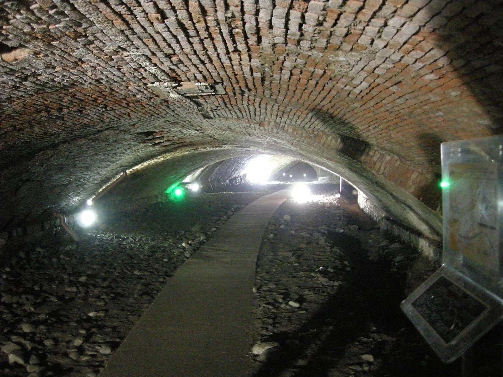 Galleria con volta in mattoni e passerella illuminata nel percorso di Pistoia Sotterranea